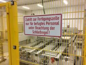 Safety cell around CNC machine with warning sign